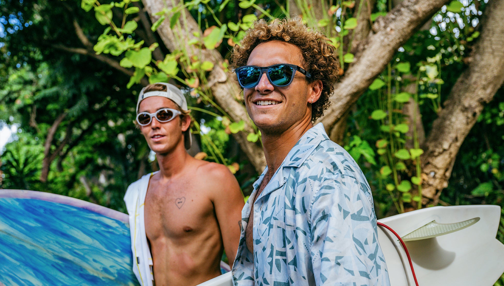Two men wearing sunglasses with surfboards standing in a forested area