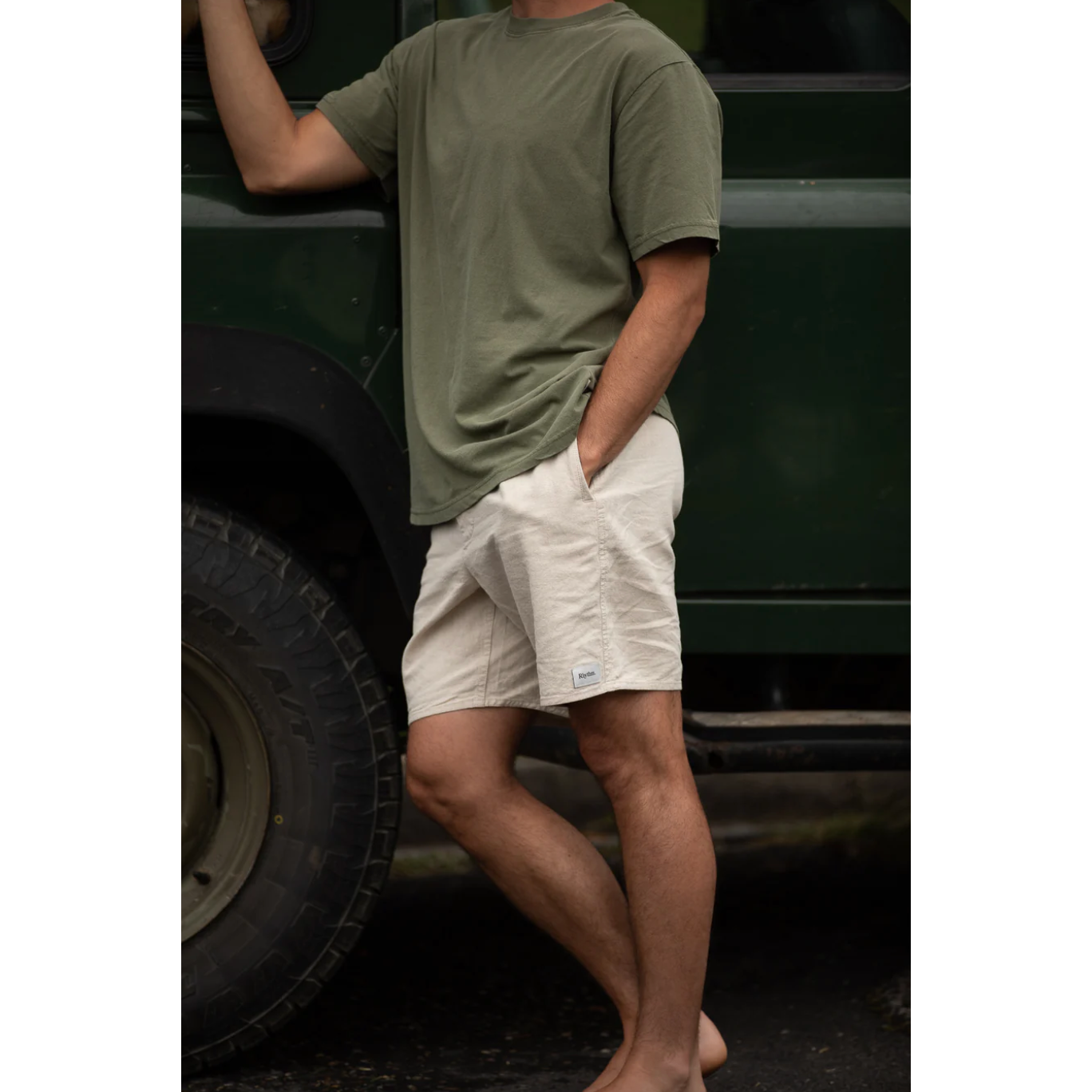 Person wearing a green t-shirt and beige shorts standing next to a vehicle.