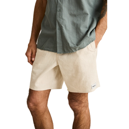 Person wearing beige shorts and a green button-up shirt on a plain background