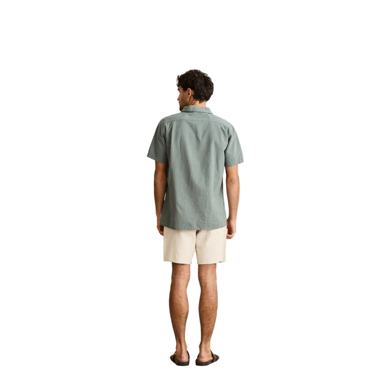 Man wearing a light green shirt and beige shorts standing against a plain background