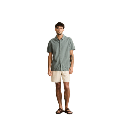 Man wearing a green button-up shirt and beige shorts against a plain background